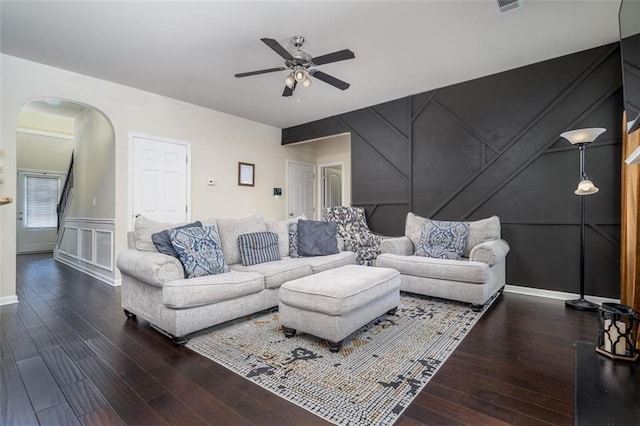 living area with arched walkways, a decorative wall, ceiling fan, and wood finished floors