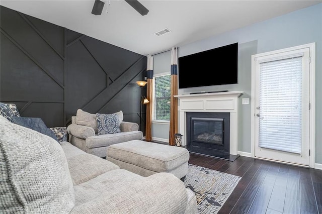 living area with visible vents, a glass covered fireplace, dark wood finished floors, baseboards, and ceiling fan