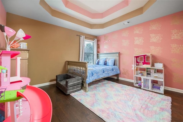 bedroom with visible vents, baseboards, a tray ceiling, and wood finished floors