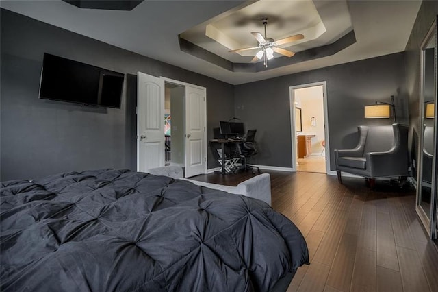 bedroom featuring a raised ceiling, wood finished floors, connected bathroom, baseboards, and ceiling fan