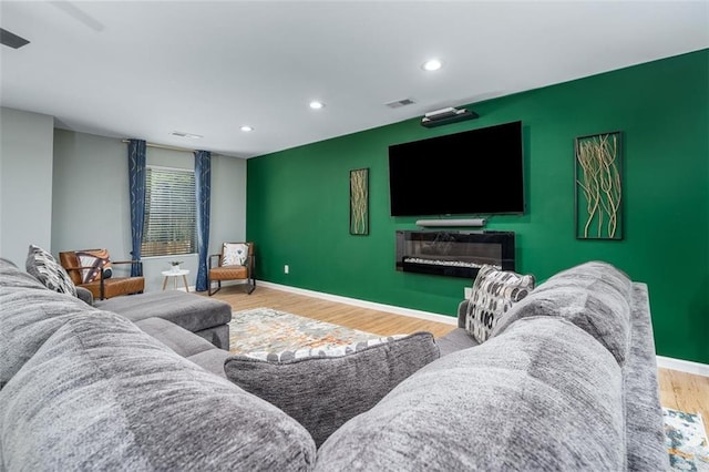 living area featuring an accent wall, wood finished floors, visible vents, and baseboards