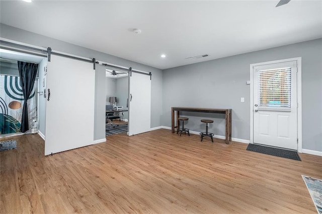 unfurnished living room featuring a barn door, light wood-style floors, baseboards, and visible vents