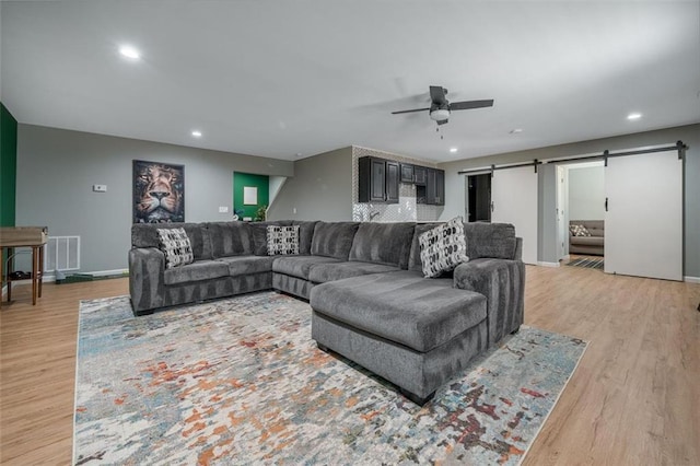 living area with visible vents, a ceiling fan, light wood-type flooring, and a barn door