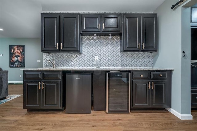 kitchen with light wood-type flooring, beverage cooler, backsplash, baseboards, and dark cabinets