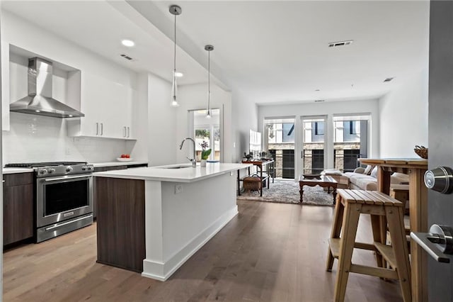 kitchen featuring wall chimney exhaust hood, pendant lighting, sink, gas stove, and dark brown cabinetry