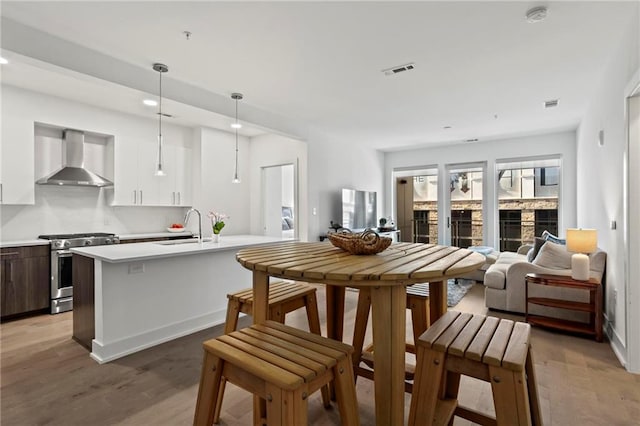 kitchen with stainless steel range with gas stovetop, white cabinets, pendant lighting, wall chimney exhaust hood, and sink