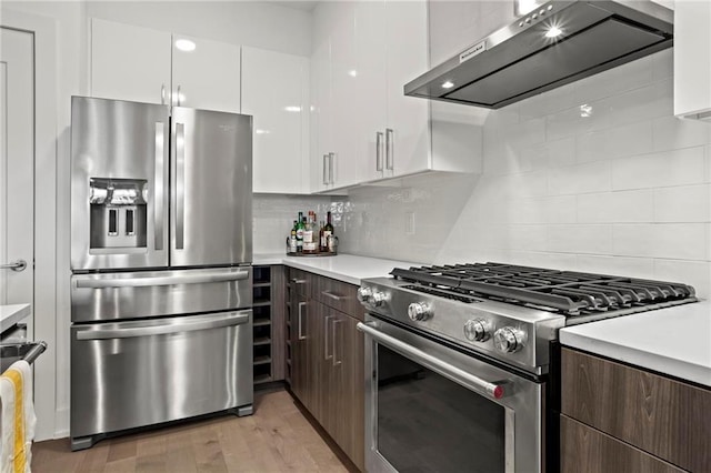 kitchen featuring wall chimney exhaust hood, decorative backsplash, white cabinetry, appliances with stainless steel finishes, and dark brown cabinets