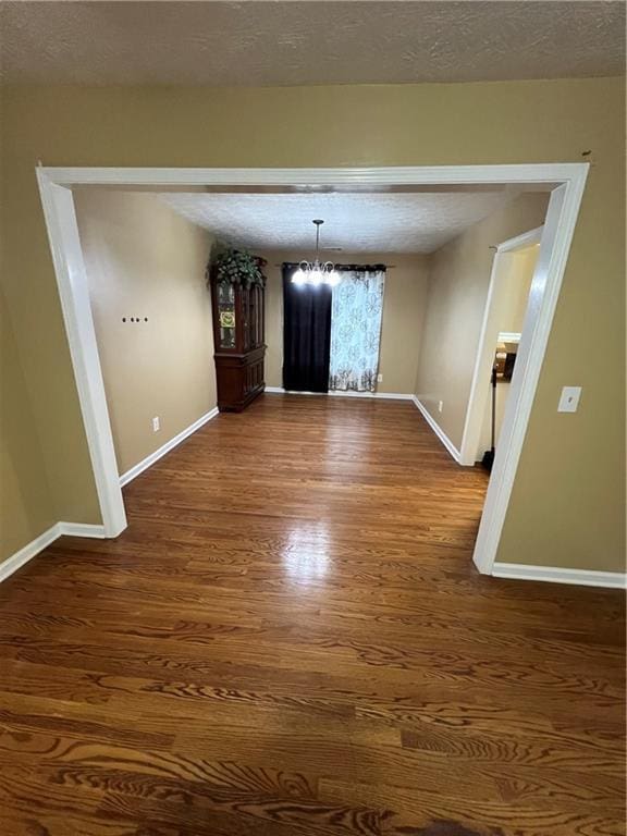 unfurnished dining area with baseboards, a textured ceiling, a notable chandelier, and dark wood finished floors