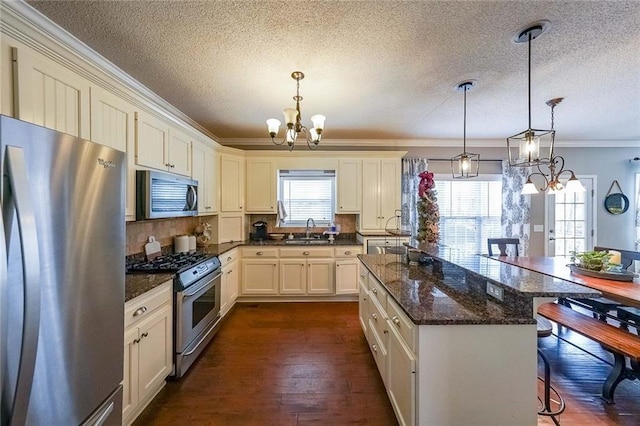 kitchen with sink, dark wood-type flooring, hanging light fixtures, a breakfast bar, and appliances with stainless steel finishes