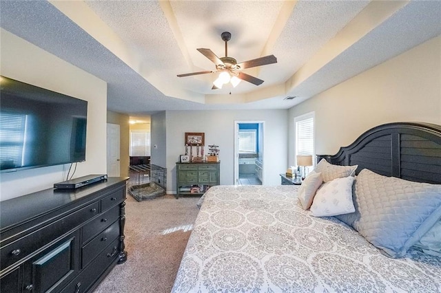 bedroom featuring light carpet, ensuite bath, ceiling fan, a textured ceiling, and a tray ceiling