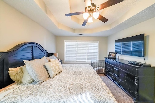 carpeted bedroom with ceiling fan and a tray ceiling