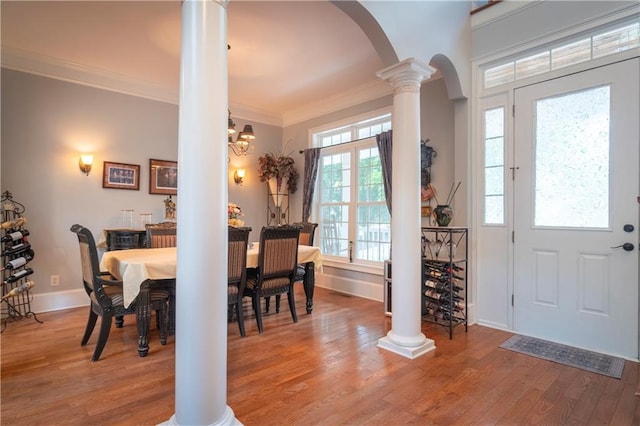 dining space featuring wood-type flooring, ornate columns, ornamental molding, and a notable chandelier