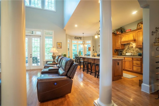 living room with a high ceiling, light wood-type flooring, an inviting chandelier, and french doors