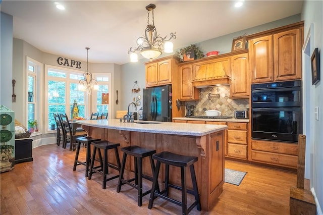 kitchen with premium range hood, an inviting chandelier, black appliances, a center island with sink, and a breakfast bar area