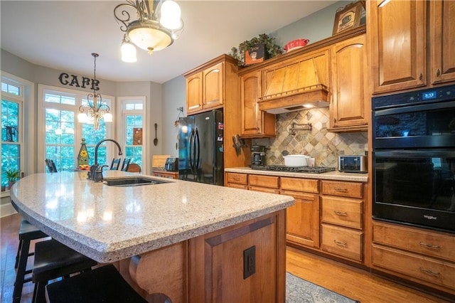 kitchen featuring backsplash, an inviting chandelier, black appliances, sink, and an island with sink