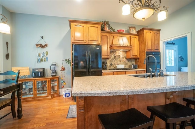 kitchen with light hardwood / wood-style flooring, premium range hood, backsplash, decorative light fixtures, and black appliances