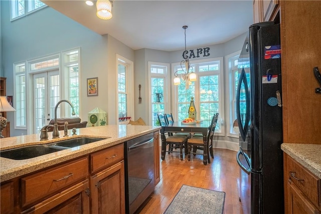 kitchen with stainless steel dishwasher, black refrigerator, light stone countertops, and sink