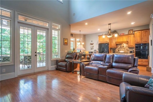 living room with a towering ceiling, french doors, an inviting chandelier, and light hardwood / wood-style flooring