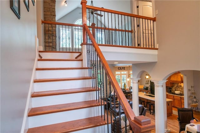 staircase featuring ornate columns, high vaulted ceiling, a healthy amount of sunlight, and wood-type flooring