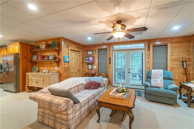 carpeted living room with a drop ceiling, ceiling fan, and wooden walls