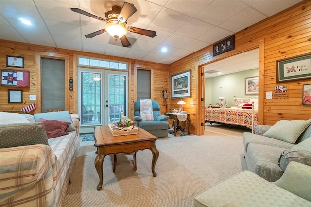 carpeted living room featuring french doors, ceiling fan, and wooden walls