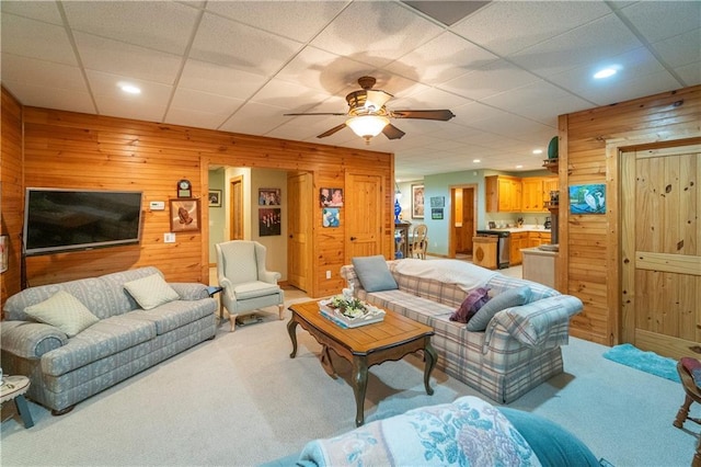 carpeted living room featuring a paneled ceiling, wood walls, and ceiling fan