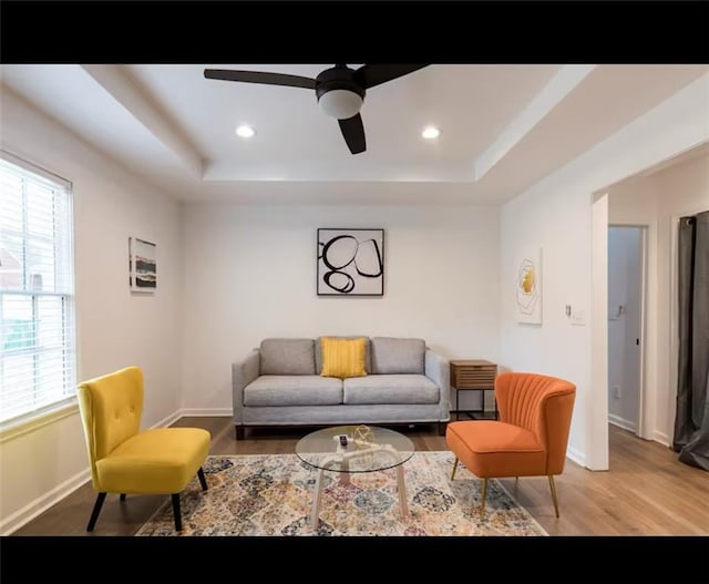 living room with light hardwood / wood-style floors, a tray ceiling, and ceiling fan