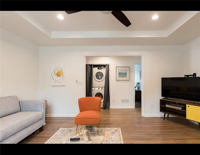 living room featuring dark wood-type flooring, ceiling fan, a tray ceiling, and stacked washer and dryer