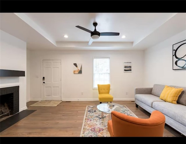 living room with a brick fireplace, hardwood / wood-style flooring, ceiling fan, and a raised ceiling