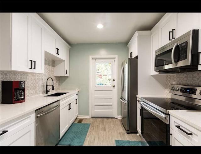 kitchen with decorative backsplash, white cabinets, light wood-type flooring, sink, and stainless steel appliances