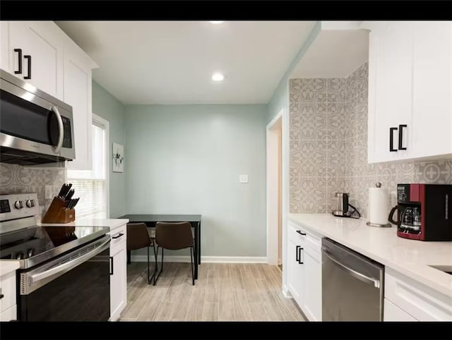 kitchen with appliances with stainless steel finishes, white cabinetry, light wood-type flooring, and backsplash