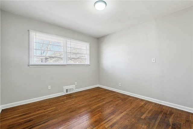 empty room featuring wood-type flooring, visible vents, and baseboards