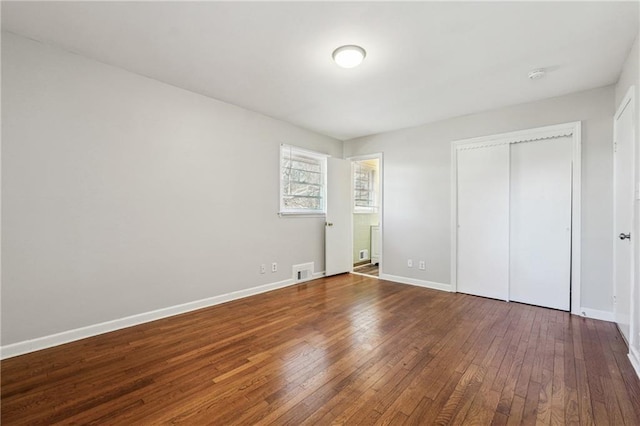 unfurnished bedroom with a closet, baseboards, visible vents, and hardwood / wood-style flooring