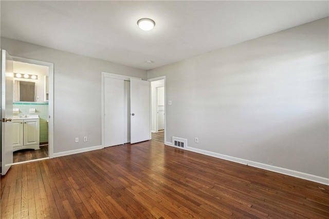 unfurnished bedroom featuring visible vents, baseboards, wood-type flooring, and ensuite bath