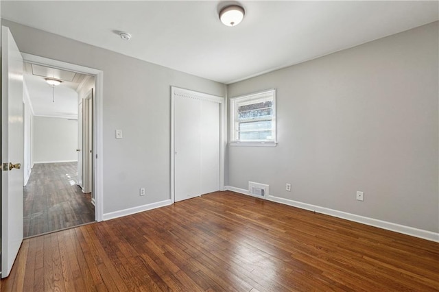 unfurnished bedroom featuring a closet, baseboards, attic access, visible vents, and hardwood / wood-style floors