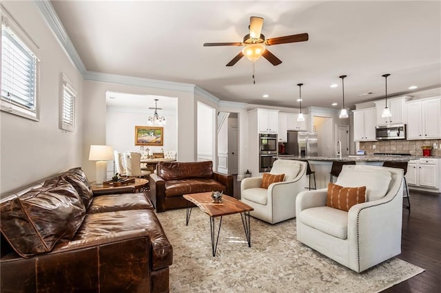 living room with ceiling fan with notable chandelier, wood-type flooring, crown molding, and sink