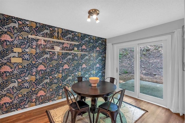 dining area featuring an accent wall, wood finished floors, baseboards, wallpapered walls, and a textured ceiling