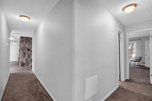 hallway with carpet floors, a textured ceiling, and baseboards