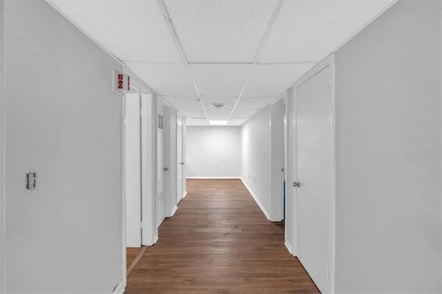 hallway featuring baseboards, a paneled ceiling, and wood finished floors