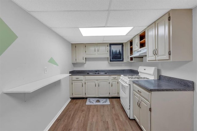 kitchen with dark countertops, white range with gas stovetop, a paneled ceiling, under cabinet range hood, and a sink