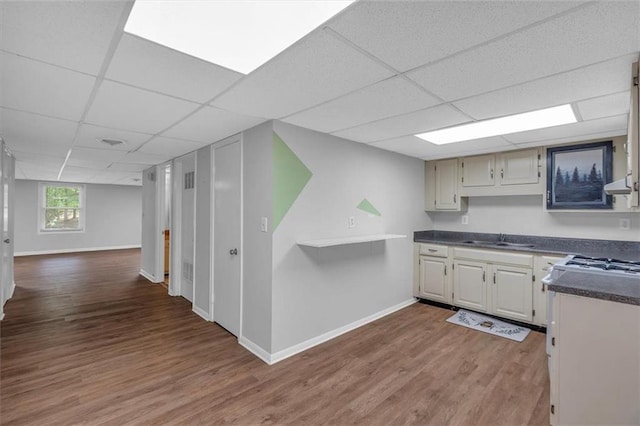 kitchen featuring a paneled ceiling, dark countertops, wood finished floors, a sink, and baseboards