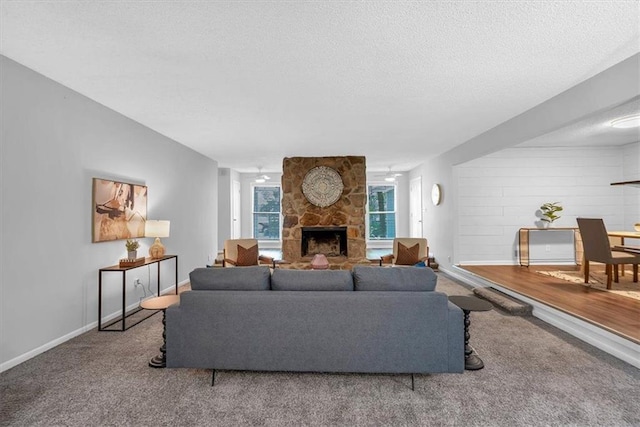 carpeted living area featuring baseboards, a stone fireplace, and a textured ceiling