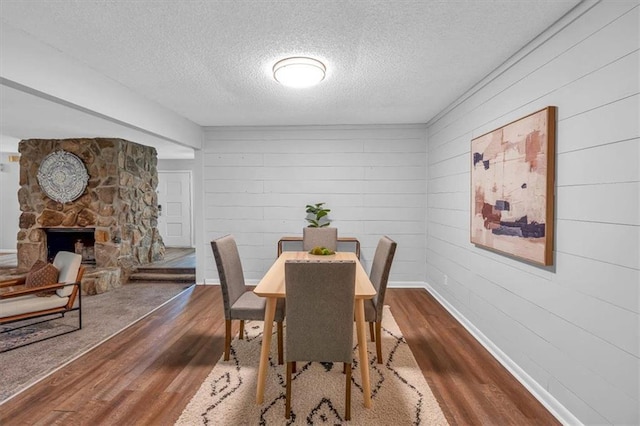 dining room with a textured ceiling, dark wood finished floors, baseboards, and a fireplace