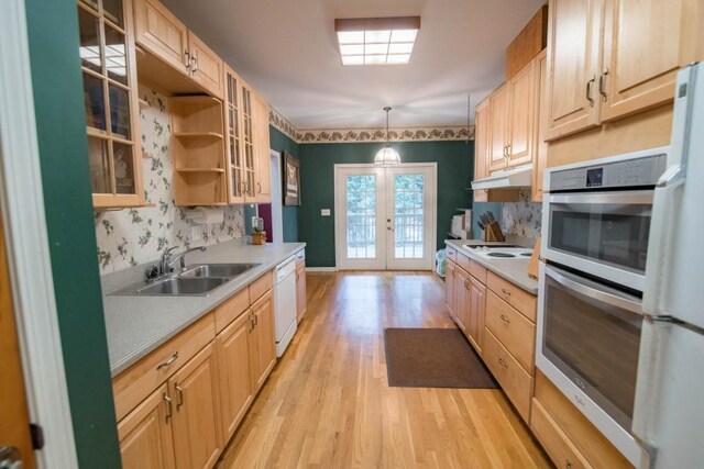 kitchen featuring light wood-type flooring, pendant lighting, french doors, sink, and white appliances