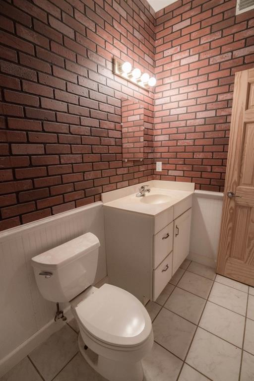 bathroom with vanity, toilet, brick wall, and tile patterned flooring