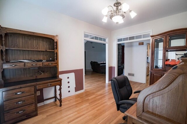 home office with light hardwood / wood-style floors and an inviting chandelier