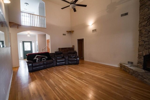 living room featuring a fireplace, ceiling fan, a high ceiling, and light wood-type flooring