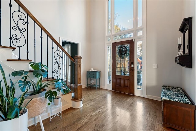 entryway featuring stairs, a towering ceiling, baseboards, and wood finished floors