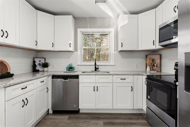 kitchen with light stone countertops, tasteful backsplash, stainless steel appliances, sink, and white cabinets