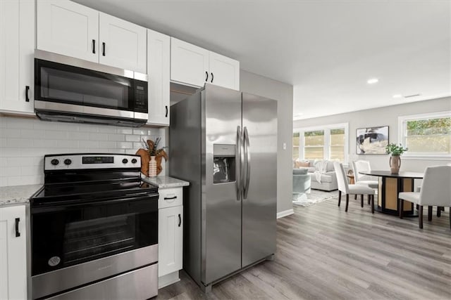 kitchen with decorative backsplash, light stone counters, white cabinets, and appliances with stainless steel finishes